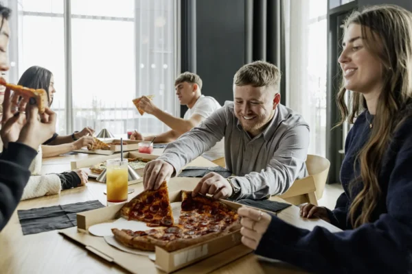 Residents sharing pizza around a long communal table in the resident lounge at Vita Living Circle Square North