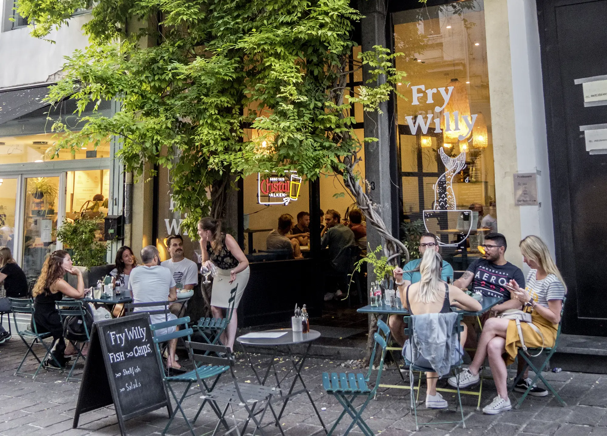 Diners at outdoor tables on a tree-shaded café terrace