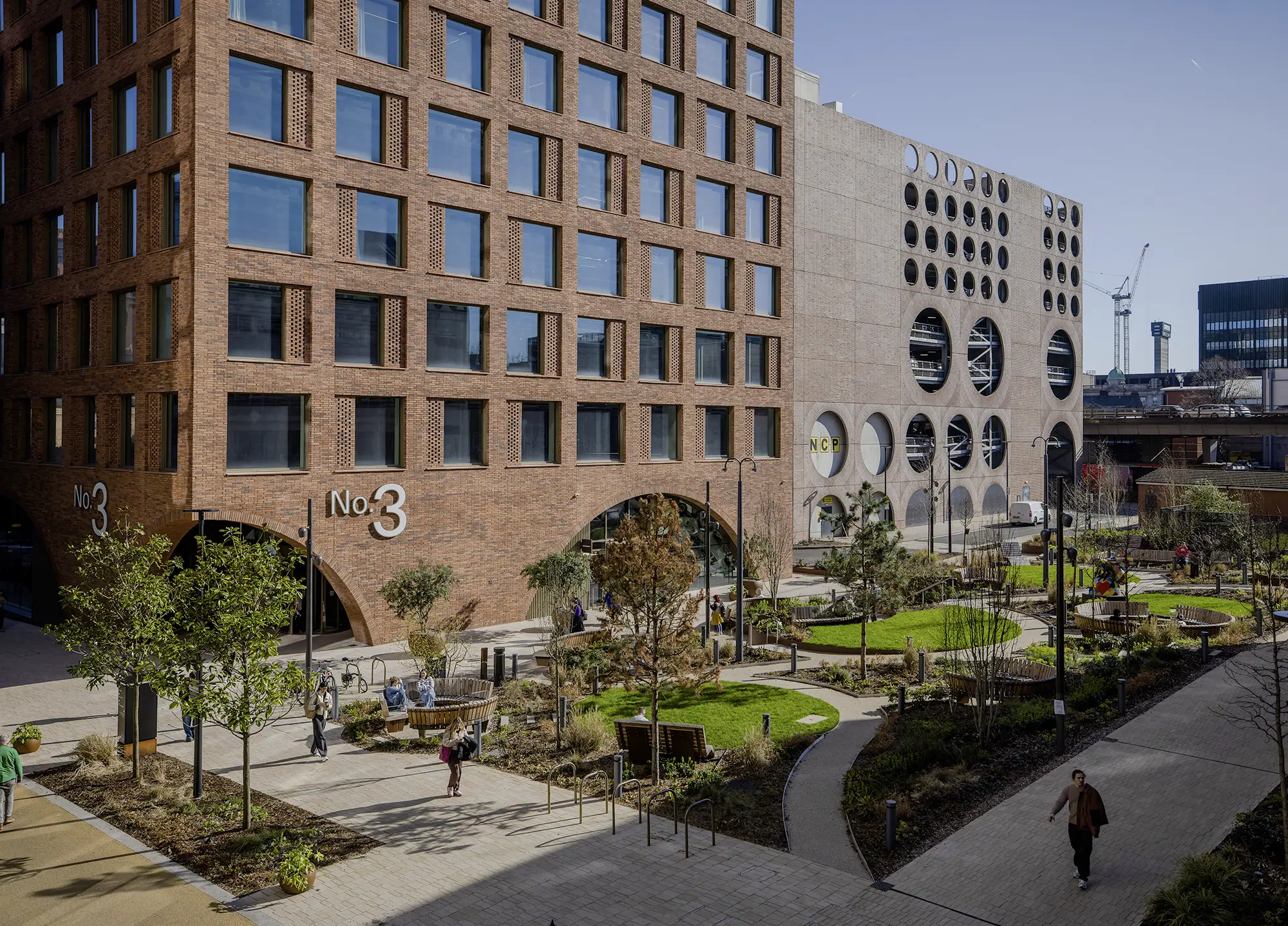 No.3 Circle Square, a red-brick office building in Manchester, seen across the development's landscaped public gardens